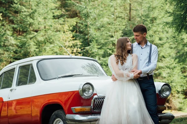 Glückliches Luxus-Hochzeitspaar küsst und umarmt sich in der Nähe von Retro-Auto. — Stockfoto