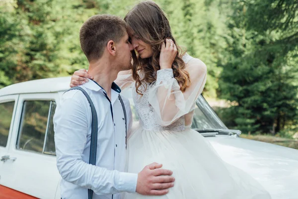 Glückliches Luxus-Hochzeitspaar küsst und umarmt sich in der Nähe von Retro-Auto. — Stockfoto