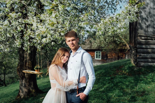 Porträt einer Braut und Paare in Hochzeitskleidung, ein weißes Kleid einen Hintergrund tsvetuschago Garten, verliebt umarmen sie und posieren. — Stockfoto