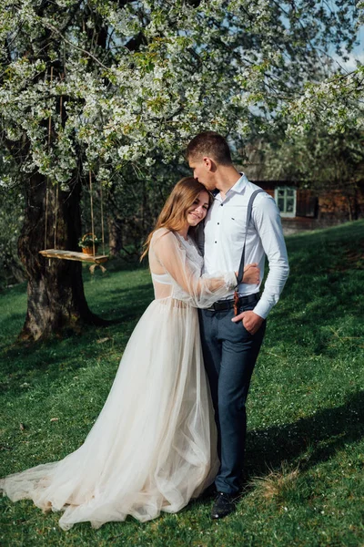 Porträt einer Braut und Paare in Hochzeitskleidung, ein weißes Kleid einen Hintergrund tsvetuschago Garten, verliebt umarmen sie und posieren. — Stockfoto