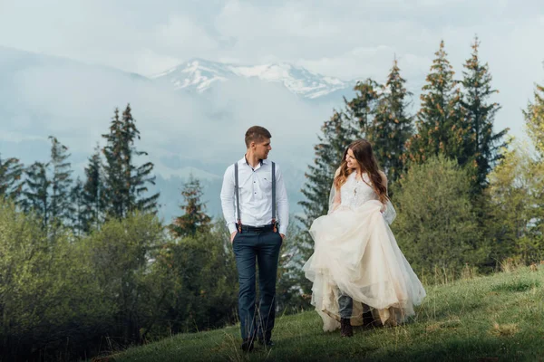 Красива весільна пара, наречена і наречений, закохані на тлі гір. Наречений в красивому костюмі і наречена в білій розкішній сукні. Весільна пара йде пішки . — стокове фото