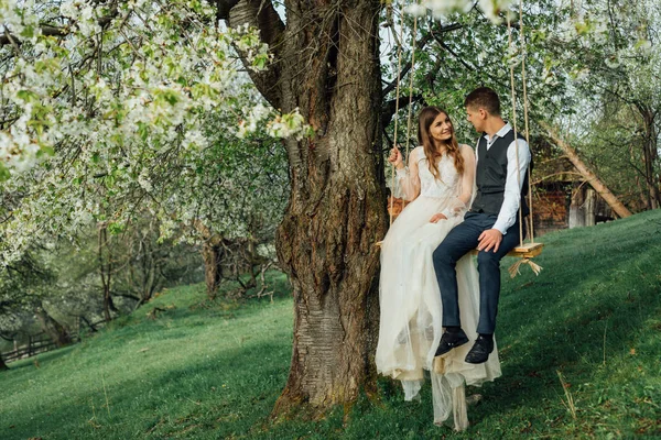 Braut und Bräutigam reiten auf einer Seilschaukel im Garten. Hochzeit im Wald. — Stockfoto