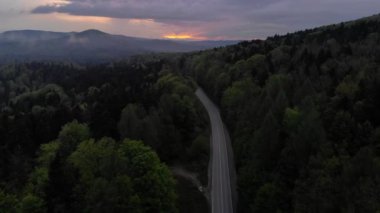 Dağ yolu ve günbatımında orman olan bir hava aracı videosu.