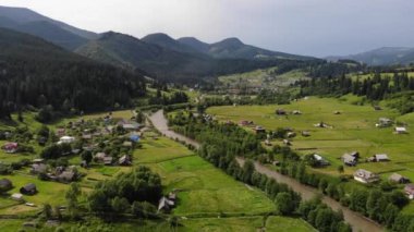 Hava Manzarası: Nehir boyunca kurulmuş güzel bir dağ köyü. Yeşil çayırlar ve çam ağaçları olan dramatik yaz manzarası. Karpatlar, Ukrayna, Avrupa. 4k