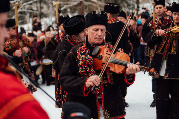 Kryvorivnia, Ukraine - January 7, 2019: Violin player in national Hutsul costume plays traditional old carol song while other men sing during Christmas celebration in Ukrainian Carpathian Mountains.