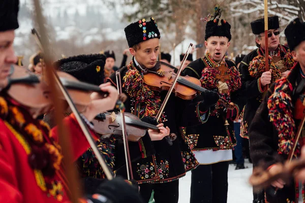 Kryvorivnia, Oekraïne - 7 januari 2019: Vioolspeler in nationaal Hutsul-kostuum speelt traditioneel oud kerstliedje terwijl andere mannen zingen tijdens kerstviering in de Oekraïense Karpaten. — Stockfoto