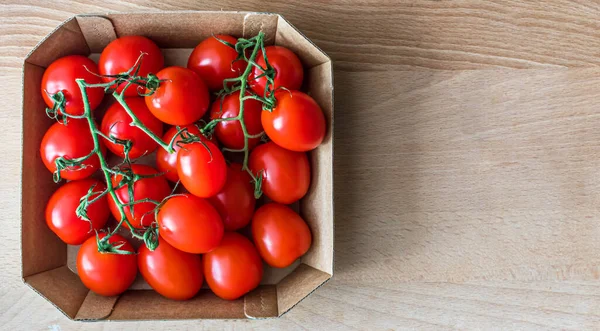 cherry tomatoes in a cardboard box on a wooden background. Fresh tomatoes with copy space, place for text top view