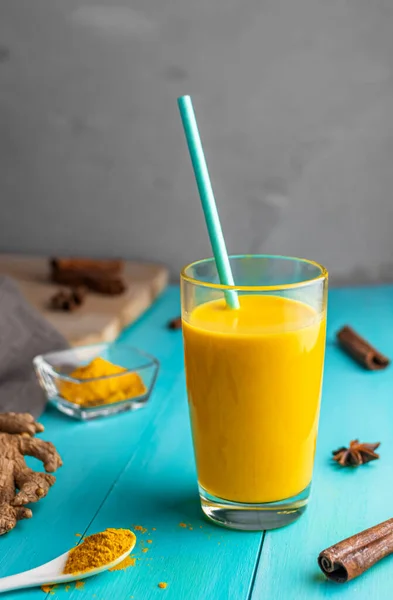 golden milk, milk with turmeric, spices. with a drinking tube. on a blue wooden background.