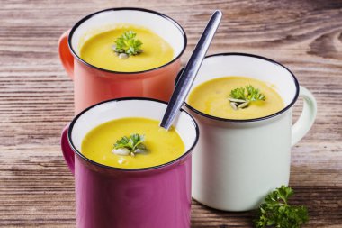 Emaye kupalar, krem ve tohumlar üzerinde ahşap bir masa ile kabak çorbası