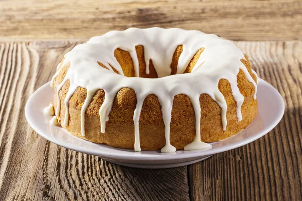 Frisch glasierter Kuchen auf weißem Teller, hölzerner Hintergrund — Stockfoto