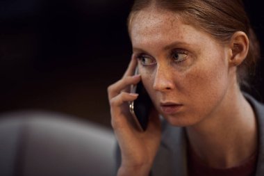 Genç kızıl saçlı iş kadını cep telefonuyla çok ciddi konuşuyor.