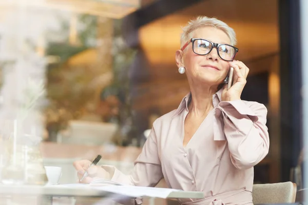 Érett Üzletasszony Szemüvegben Mobiltelefonnal Beszél Miközben Dokumentumokkal Dolgozik Asztalnál — Stock Fotó