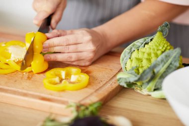 Genç bir kadın mutfakta salata yemek için tahtada sebze kesiyor.