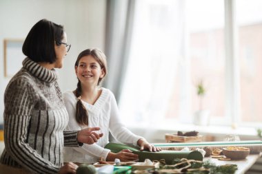 Gülümseyen kız yeşil ambalaj kağıdıyla süsleme kutusu ve evde annemle konuşuyor.