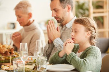 Üç kişilik aile yemek masasında gözleri kapalı oturup evde yemek yemeden önce dua ediyorlar.