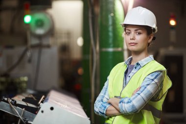 Portrait of female foreman in protective workwear standing with arms crossed and looking at camera while working in the plant