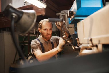 Serious bearded mechanic working on machine in the factory 
