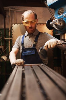Young worker in protective glasses working on lathe in the factory 