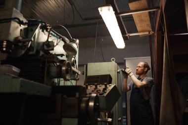 Young mechanic in work wear standing near the lathe and working on factory
