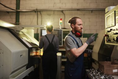 Manual worker in work wear examining the metal details and produced on the metal factory