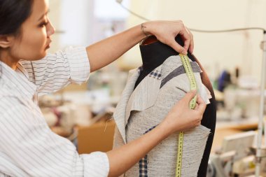 Asyalı terzi atölyede dikiş dikerken ceketten manken ölçümü alıyor.