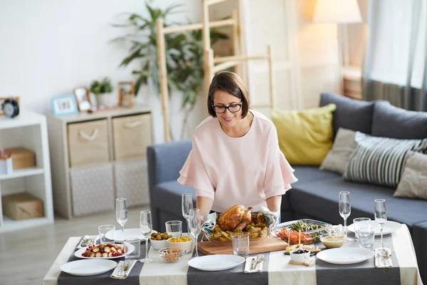 眼鏡の若い女性は ダイニングテーブルの上にロースト七面鳥を置き リビングルームでの休日の夕食の準備 — ストック写真