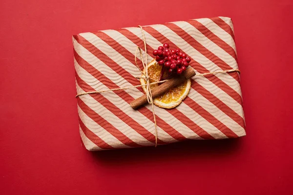 빨간색 배경에 열매와 계피로 장식된 줄무늬 포장지로 장식된 크리스마스 상자의 — 스톡 사진