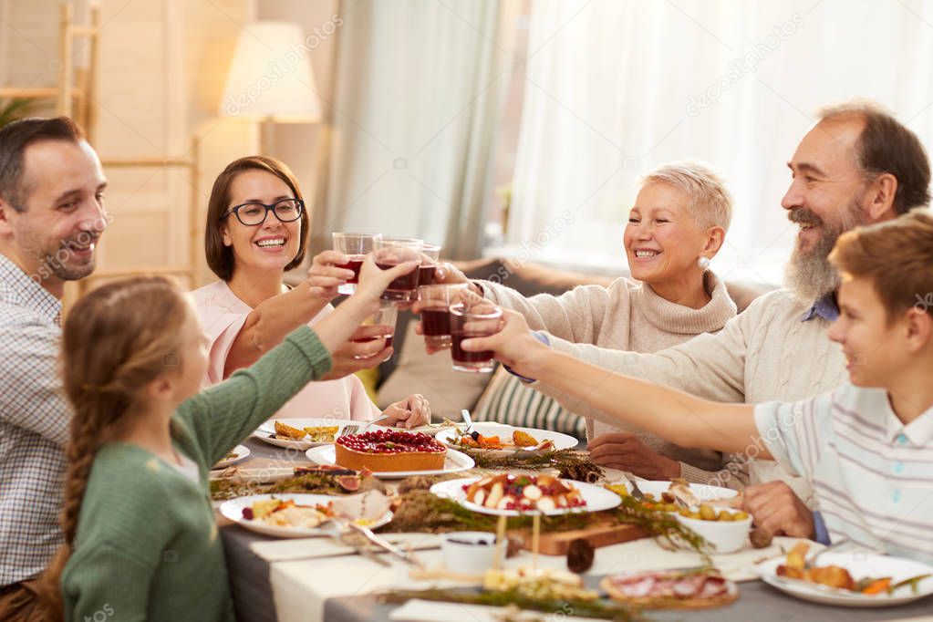 Happy big family sitting at dining table and toasting with red wine together while celebrating holiday at home