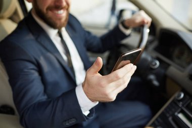 Close-up of young man holding mobile phone reading message and smiling while sitting behind the wheel