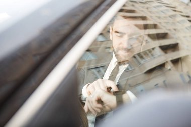 Young businessman sitting in the car and checking the time on the wristwatch
