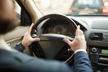 Rear view of young man sitting and holding the wheel of the car during driving