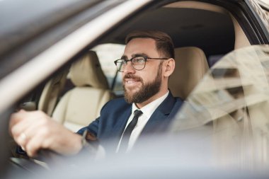 Successful young businessman in eyeglasses driving car and smiling