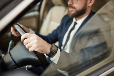 Young successful businessman in eyeglasses and in suit sitting in luxury car and driving 