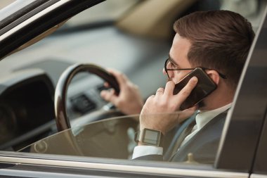 Young businessman in eyeglasses talking on mobile phone and driving the car 