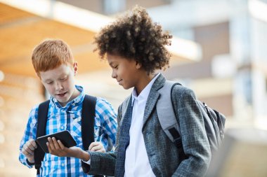 Two boys in casual clothing  using mobile phone together after school outdoors