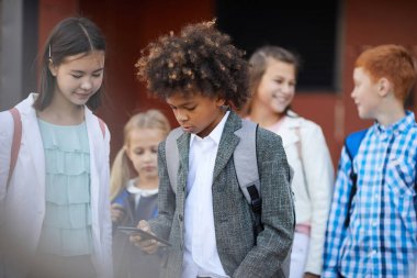 African schoolboy using mobile phone while standing with classmates outdoors