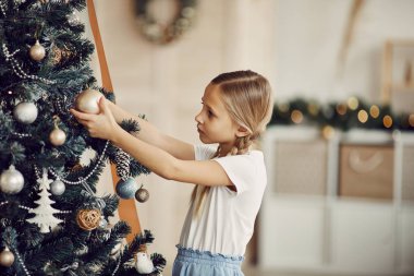 Evdeki Noel ağacında duran ve oyuncakları inceleyen sevimli küçük kız.