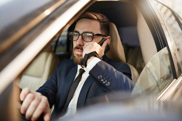 Бизнесмен в очках за рулем и разговаривает по телефону