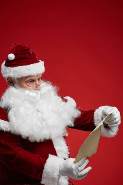 Noel Baba gözlük takıyor ve kırmızı arka planda el ele mektup okuyor.