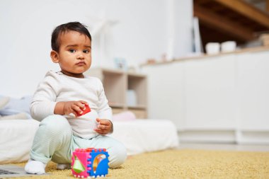 Cute African baby boy looking at camera while sitting on the floor and playing with toys at home