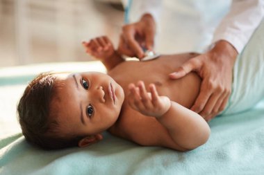 African newborn lying on back while doctor listening to heartbeat with stethoscope at hospital