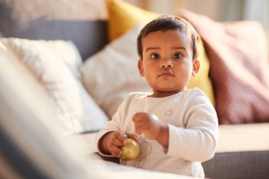 Portrait of child standing near sofa and holding toy and looking at camera in domestic room at home