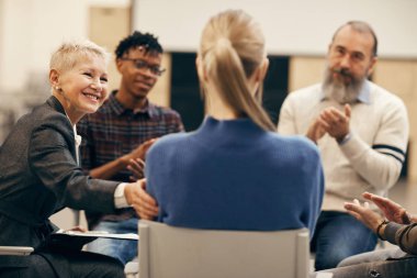Rear view of young blond woman sitting and telling story to other people in therapy class