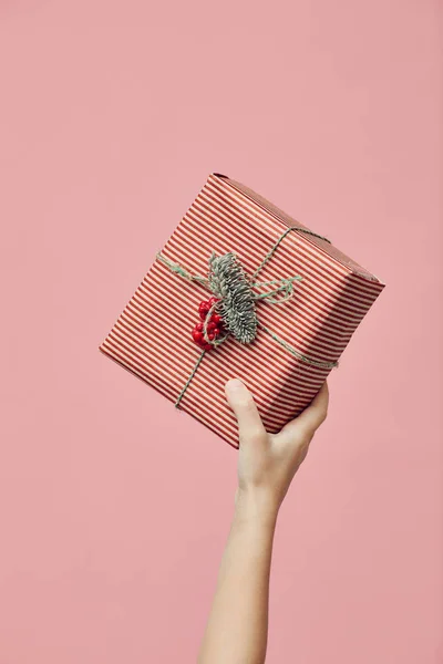 Close-up of female hand raising Christmas present up over pink background