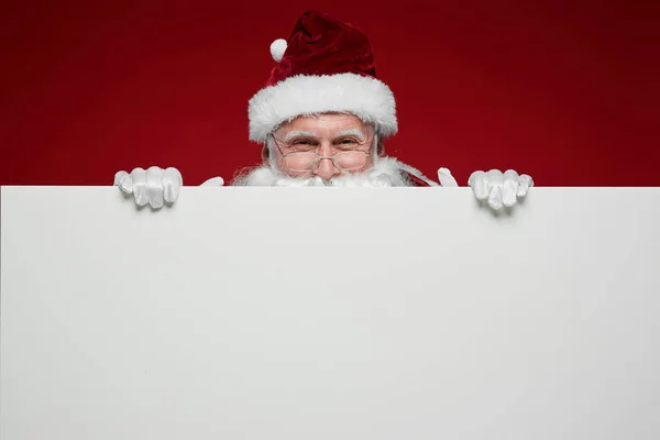 圣诞老人的画像 戴着眼镜 戴着帽子 对着相机微笑 拿着大大的白色海报 — 图库照片