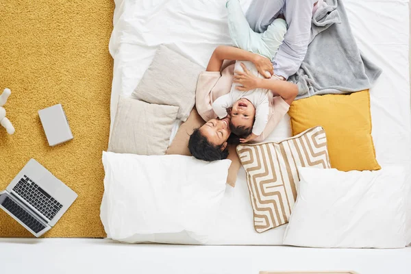High angle view of happy young mother lying and embracing child in the bed in the bedroom at home