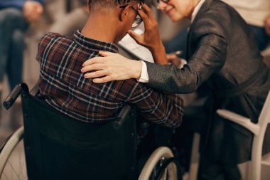Afrikalı genç bir adamın tekerlekli sandalyede oturması ve olgun bir kadının desteğiyle sağlığından endişe etmesi.