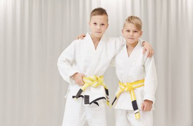 Kimono giymiş iki judocunun birbirlerine sarılıp kameraya baktıkları portresi.