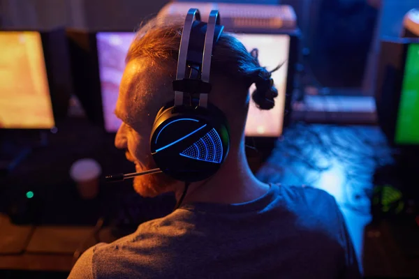 헤드폰을 백라이트를 컴퓨터 게임을 어두운 방에서 젊은이의 뒷모습 — 스톡 사진