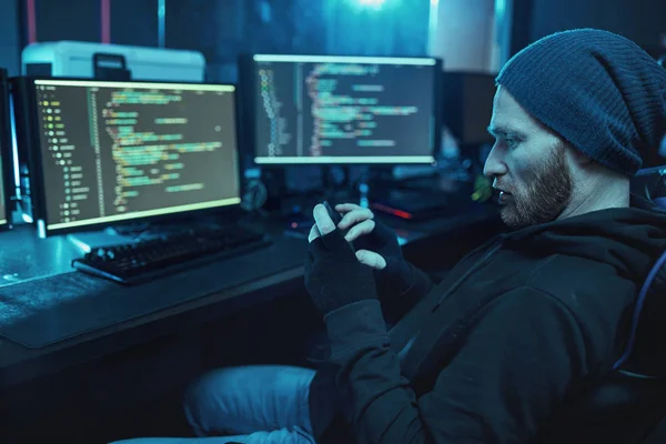 Brodaty Młody Haker Kapeluszu Bluzie Kapturem Siedzi Przed Monitorami Komputerowymi — Zdjęcie stockowe